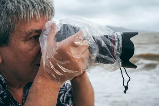 professional male photographer takes pictures with digital camera in a protective case waterproof plastic bag against splashing rain in nature