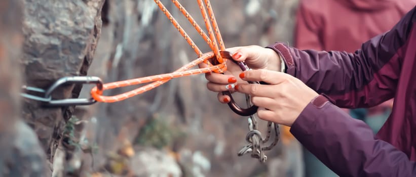 Climbing station on bolts on a rock, people are learning mountaineering in a camp outdoor, a woman's hand checks the reliability of belay, rope, carabiners.