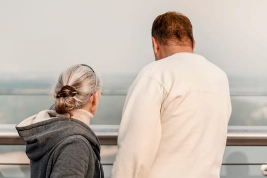 A man and a woman are walking in the park and talking, looking at a beautiful city view - a panorama. Husband and wife aged happily spend time together and support each other.