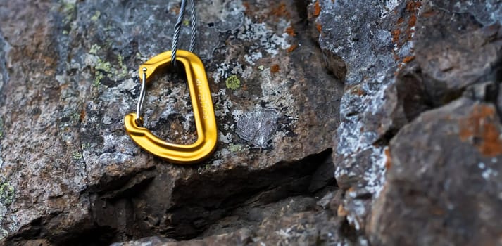 Climbing equipment, the yellow carabiner at the belay station lies on the rock.