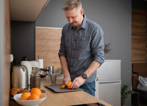 Happy Man Cutting Orange At Home In The Kitchen