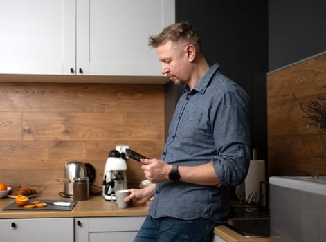 Man Looking At Smartphone In Kitchen At Home