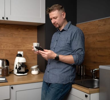Man Looking At Smartphone In Kitchen At Home