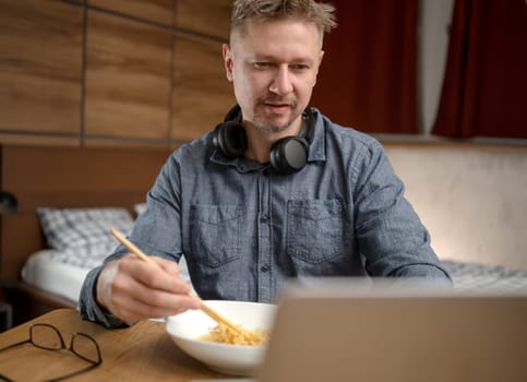Charming Man Eating Noodles With Chopsticks Watches News On Laptop