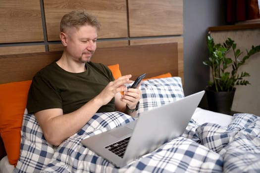 In The Morning, A Man Lying In Bed With A Laptop And Smartphone At Home