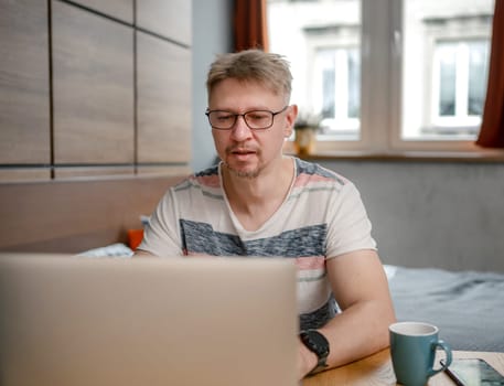 Man Working Remotely On Laptop At Home In Bedroom