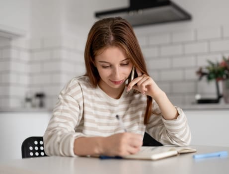 Girl Talks On Phone And Writes In Notebook At Home