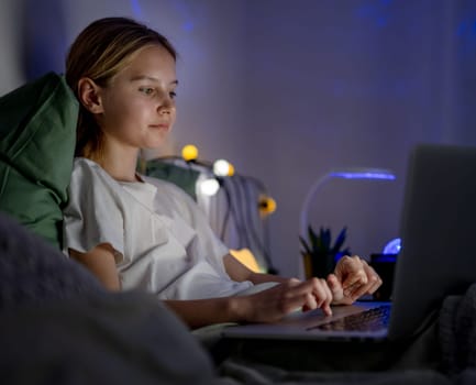 Cute Little Girl In Bed Typing On Laptop Before Sleep And Sending Messages