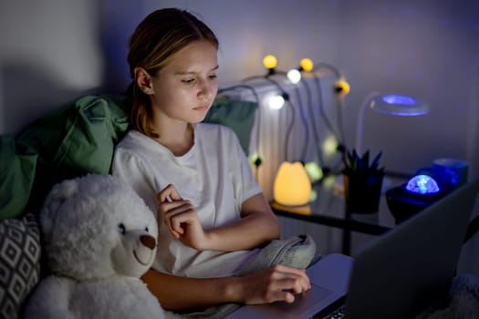 Cute Little Girl In Bed Browses The Internet On Laptop Before Sleep With Lovely Teddy Bear