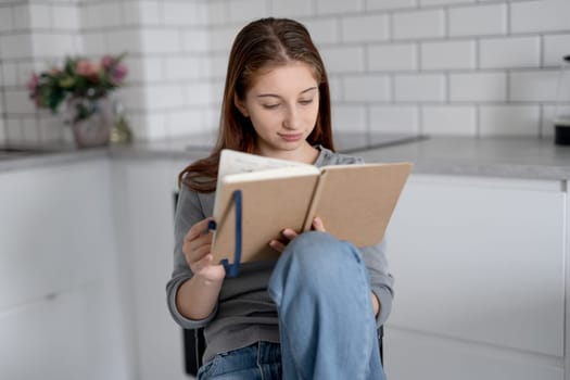 Sweet Teen Girl Reading Notebook Entries While Sitting On A Chair At Home