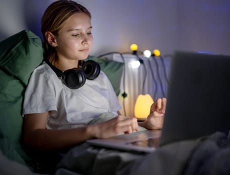 Cute Little Girl Browses The Internet And Social Media and Searching on laptop In Bed Before Sleep