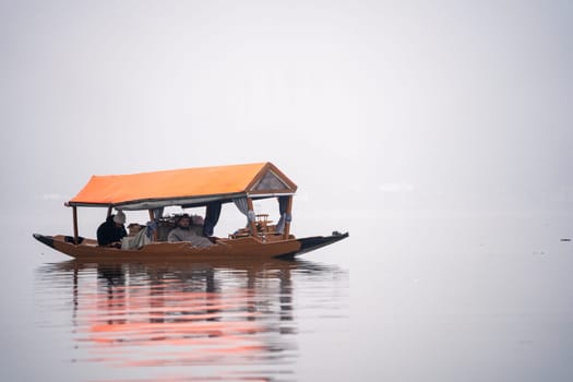 Srinagar, Kashmir - 3rd Jan 2025: Tourists sitting in wooden Shikara boats with colorful roofs on the famous dal lake covered in fog showing the popular tourist activity