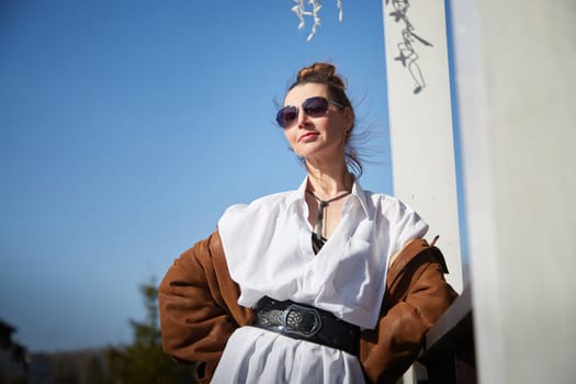 A woman stands confidently outdoors, dressed in a stylish outfit with sunglasses, showcasing a trendy look in bright daylight.