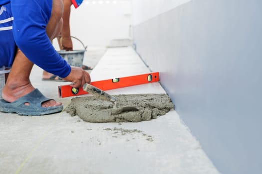 A worker smooths a layer of gray mortar, creating an even foundation for securely setting floor tiles in place.