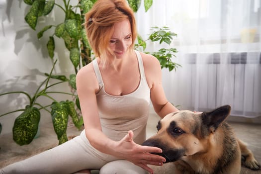 A woman practices yoga in a well-lit room surrounded by lush plants, gently interacting with her dog to emphasize a healthy lifestyle.