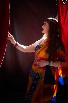 A mature woman in a colorful sari poses gracefully, highlighting her style against a dramatic backdrop, embodying a blend of culture and modernity.