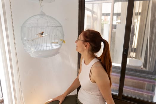 Woman admiring her zebra finch resting in its hanging cage, enjoying a peaceful moment at home