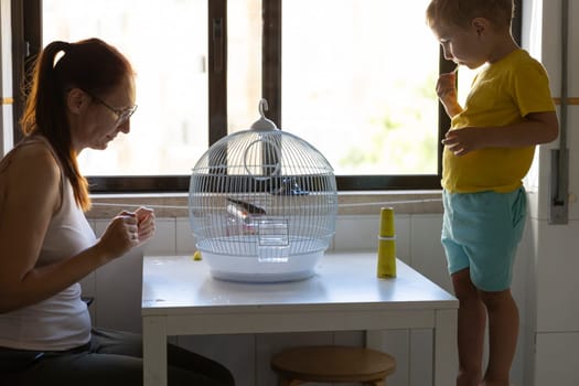Woman and child taking care of their pet bird inside a cage placed on a table