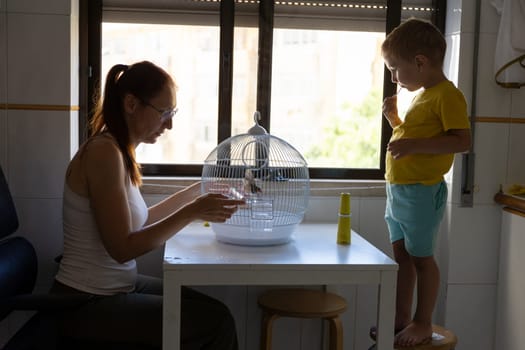 Mother taking care of pet bird while her son brushes his teeth, promoting responsible pet ownership and healthy habits within a family setting