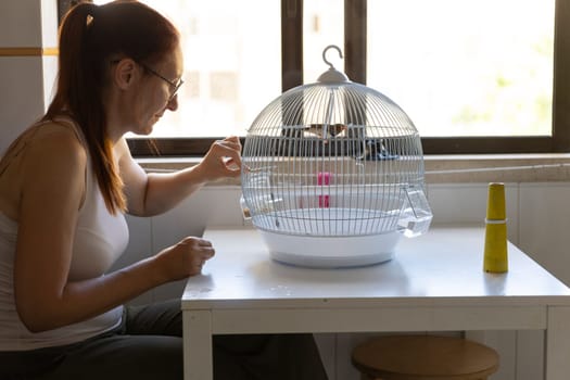 Woman taking care of her pet bird, feeding it in its cage