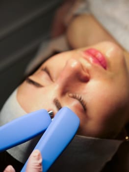 Cosmetic procedure for a woman Microcurrents for a woman's face at a beautician. Rejuvenating effect, toned skin, uniform skin color. Close-up, vertical