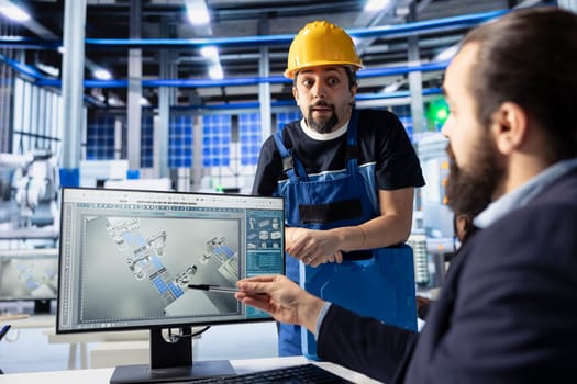 Manager in photovoltaics factory talking with worker, diagnosing malfunctioning systems, pointing to PC screen. Solar panels manufacturing plant experts doing brainstorming to reduce downtime
