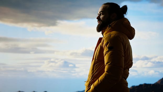 Male trekker takes in the breathtaking mountain landscape on rocks, enjoying the scenic background, crisp air and rugged peaks. Excitement of discovering new horizons. Camera B.