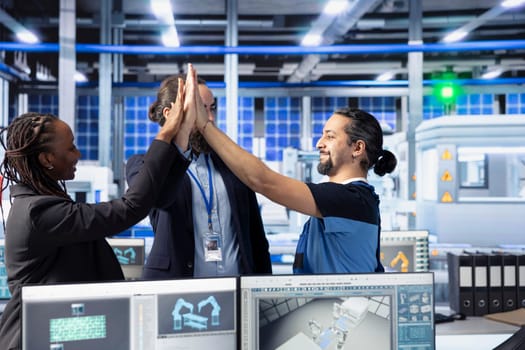 Smiling managers in photovoltaics factory doing high five, happy with performance of solar panels manufacturing. Pleased management team celebrating passing solar plant machinery inspection
