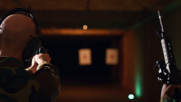 Team of army soldiers practicing with firearms in shooting range to increase firing accuracy. Military units in shooting gallery using pistols and rifles to engage targets at extended range, camera B