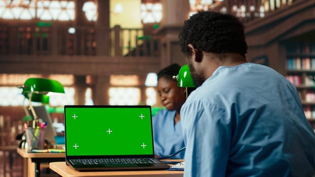 Black medical student reviews case files in the library next to copy space screen, preparing for a lecture or study session on medical practices. Med school pupil learns for a career. Camera B.