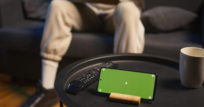 African american casual guy relaxing on the couch next to isolated screen, feeling pleased with working from home at his cool apartment. Young adult laying on the sofa, remote job. Camera B.