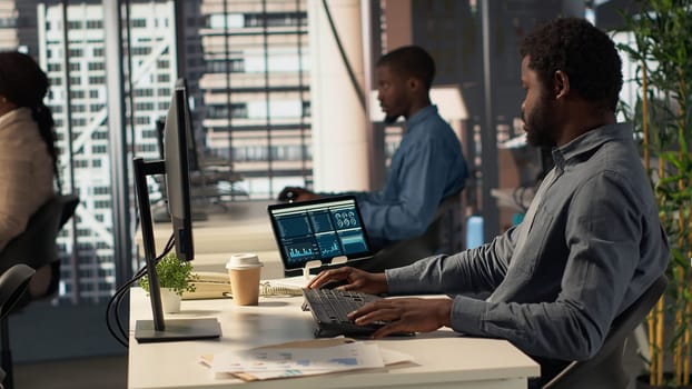 Black analyst working with monthly revenue balance to create financial plans using online tools, analyzing data infographics. Businessman managing organizational goals for efficiency. Camera A.