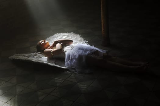 A woman dressed as an angel lies on the floor in a beam of light