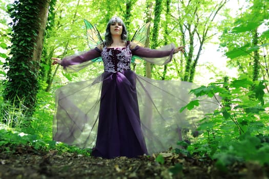 A beautiful elf with wings and a purple dress enchants a forest