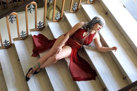 A pretty woman in a red dress lies on a white marble staircase