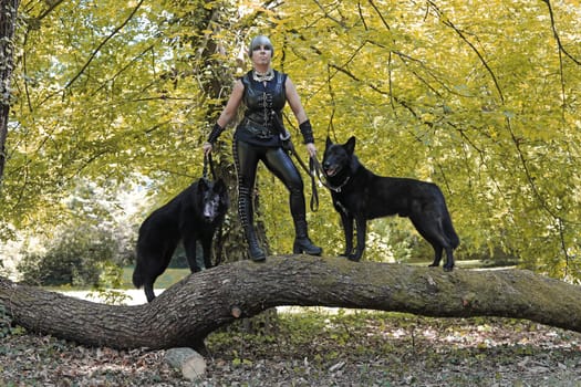 A woman dressed in black with two black dogs on a tree trunk