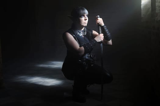 A woman disguised as a dark elf with a sword waits in the beam of light in a crypt