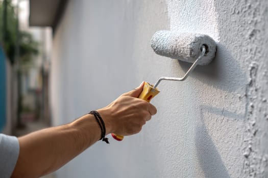 Person painting wall with roller in casual outfit. wall home background..