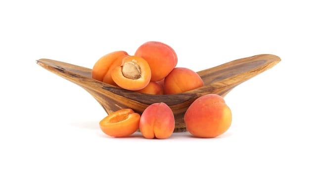 Juicy ripe apricots in a rustic wooden bowl placed against a neutral white backdrop, emphasizing freshness and simplicity.