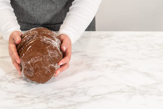 Front view of four discs of Chocolate Ginger Sugar Cookie Dough, each wrapped in plastic and stacked on a marble countertop, ready for storage or chilling.