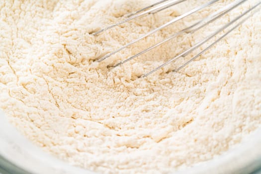 Close-up view of dry ingredients for Classic Sugar Cookie Dough, including flour and sugar, showing a textured mix in a bowl. This macro shot captures the fine details of the flour's texture, essential for the cookie dough preparation process.