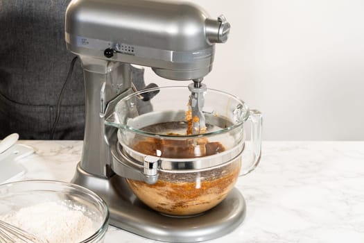Eye-level view of a stand mixer with a glass bowl, blending the ingredients for Classic Gingerbread Cookie Dough. Visible layers include the dark molasses mixture and brown sugar, ready to be combined for a rich gingerbread base.
