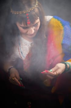 A mature blonde woman poses gracefully in a colorful sari, celebrating Indian traditions amidst a misty backdrop during a photoshoot.