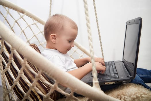 Child engages with a laptop while seated in a cozy hammock, enjoying a relaxed atmosphere indoors during the afternoon.