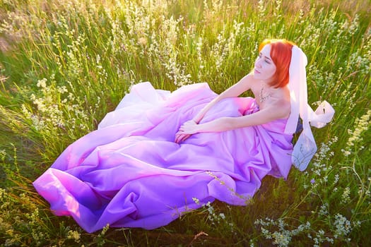 A woman with vibrant orange hair sits among tall grass and blooming flowers, wearing a flowing pink dress that blends with the colorful landscape under a warm summer sky.