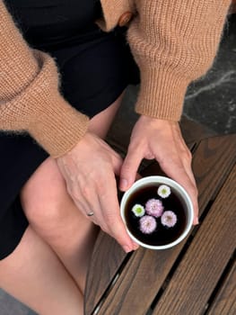 A person enjoys a cup of floral tea, showcasing delicate flowers floating on top, seated in a warm cafe.