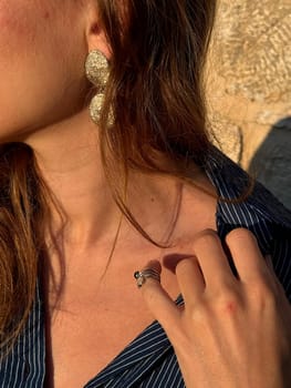 A woman is highlighting her fashionable earrings and ring while enjoying a sunny moment outdoors.