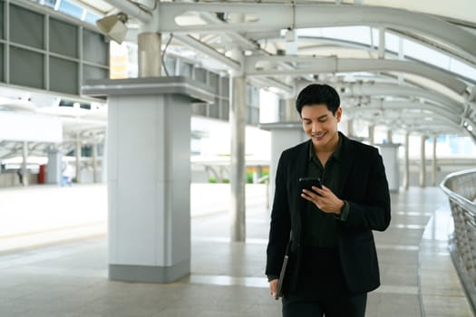 Young male executive walking through a modern walkway and checking his smartphone.