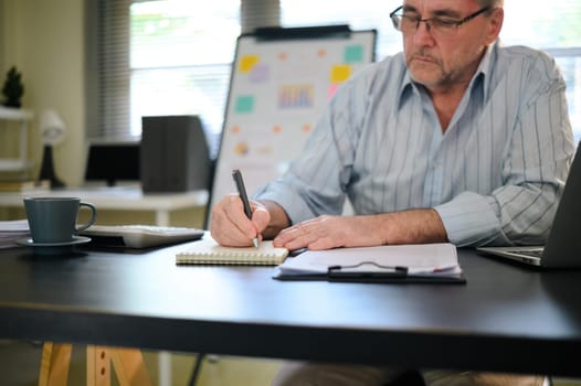 Senior businessman working at desk, writing and analyzing documents.