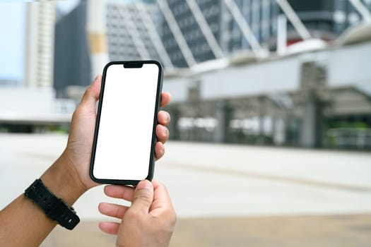 Hands holding smartphone with blank white screen in an urban cityscape.